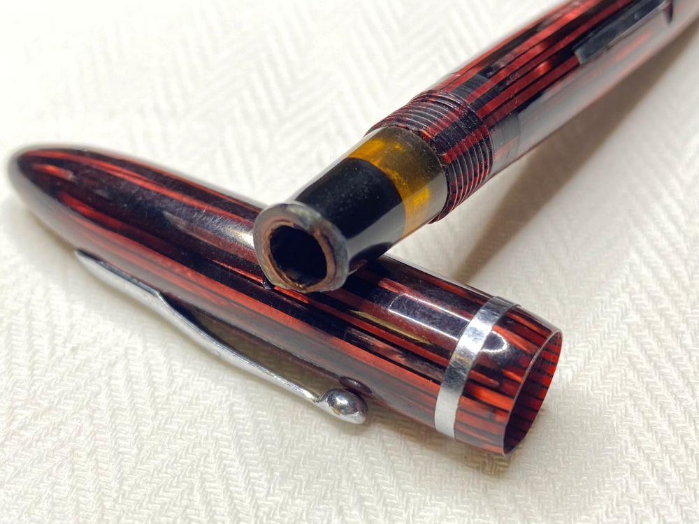 A red fountain pen, missing its nib and displaying a burned section.